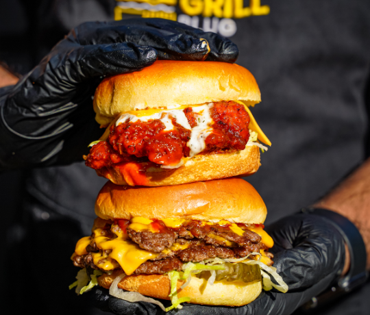 Person holding two burgers on top of each other, man is wearing a Grill Plug T shirt