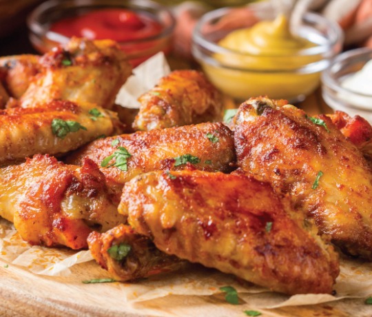 Platter of wings, with different sauces in the background to dip